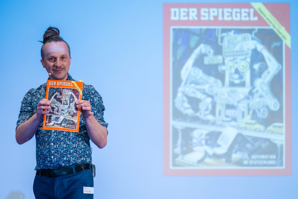 Sebastian Winkler hält auf der Bühne ein SPIEGEL-Heft hoch, Mediaan-Konferenz 2024