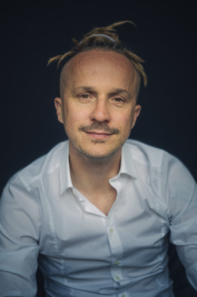Porträt von Sebastian Winkler im weißen Hemd vor dunklem Hintergrund, leichtes Lächeln
