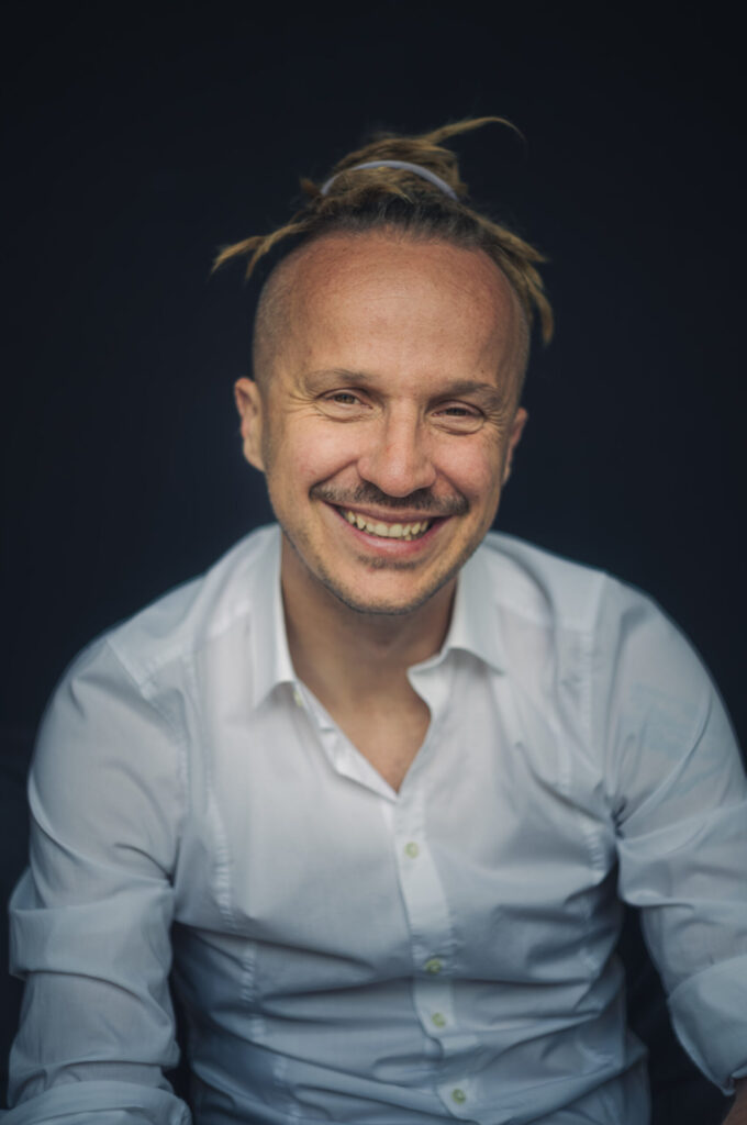 Sebastian Winkler lacht in die Kamera, weißes Hemd, dunkelblauer Hintergrund