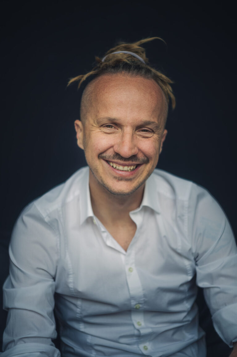 Sebastian Winkler lacht in die Kamera, weißes Hemd, dunkelblauer Hintergrund